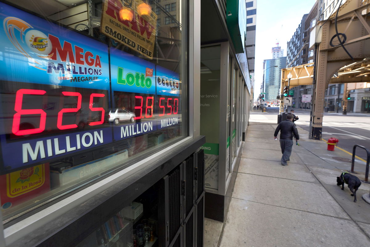 A man walks his dog past lottery signs Tuesday, Jan. 12, 2021, displaying the recent jackpot amounts in Chicago's fames Loop. Lottery players have a chance to win the largest jackpots in nearly two years as Tuesday's Mega Millions has grown to an estimated $625 million and Wednesday's Powerball to an estimated $550 million. (AP Photo/Charles Rex Arbogast)