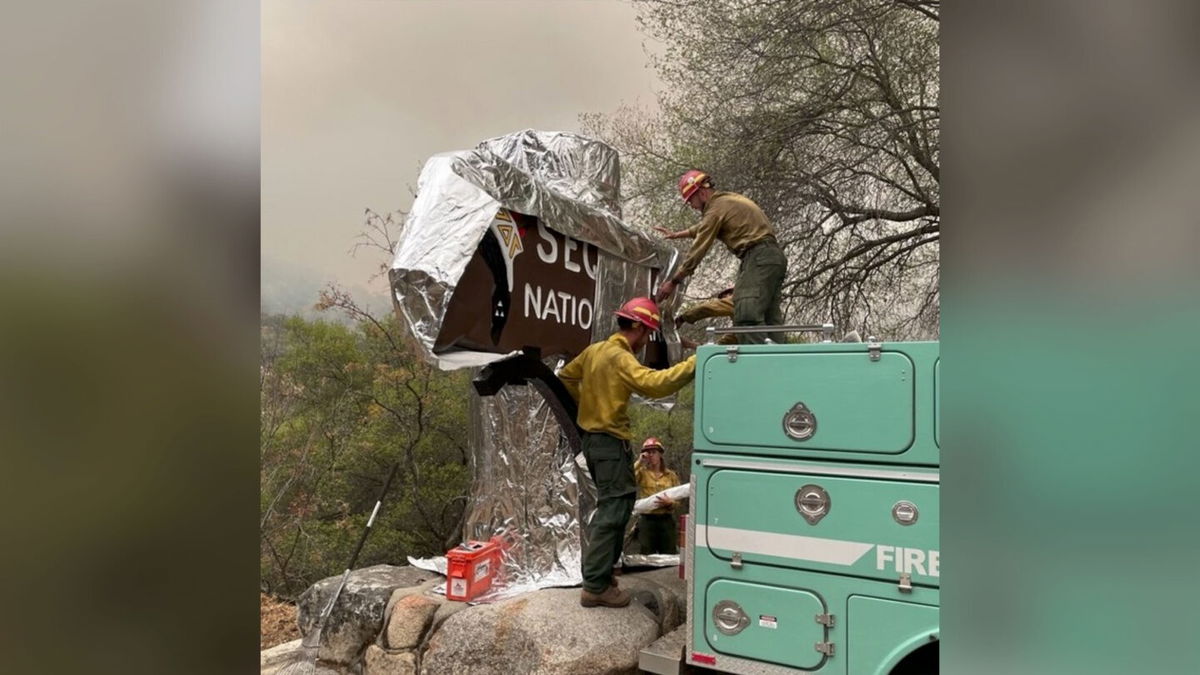 <i>From Sequoai & Kings Canyon National Parks/Instagram</i><br/>Firefighters assigned to the KNP Complex Fire prepare the historic Sequoia entrance sign for the possibility of fire in the area by wrapping it with aluminum-based burn-resistant material.