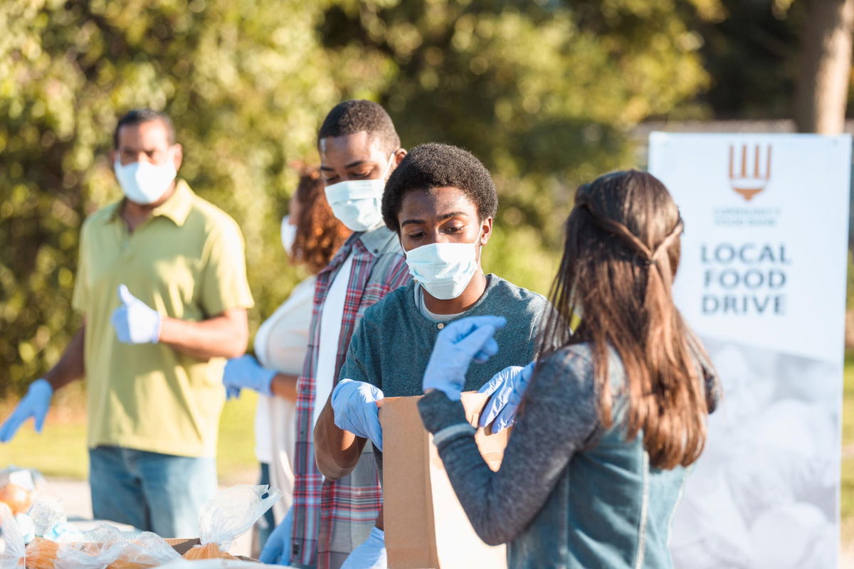 A young couple works together at the local food drive during COVID-19. Everyone wears protective masks and gloves to slow the spread of disease.