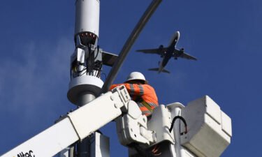 A contractor installs 5G cellular equipment on a light pole as a Delta Air Lines