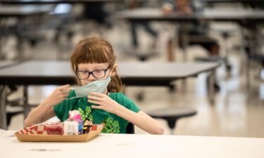 A child puts her mask back on after finishing lunch at a socially distanced table in the cafeteria of Medora Elementary School on March 17