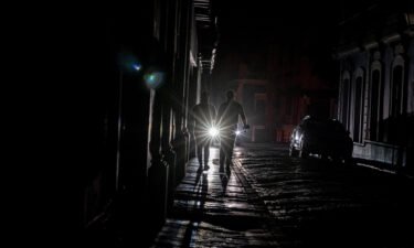 A vehicle's headlights are seen as people walk on a dark street in San Juan