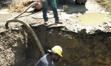 A construction worker digs out a hole around a broken 20-inch water main in Fort Worth