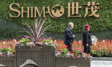 An elderly couple walk past a sign in front of Shimao Tower