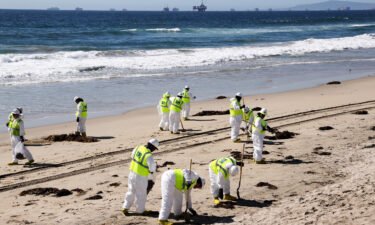 Cleanup workers search for contaminated sand and seaweed along the mostly empty Huntington Beach