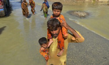 A displaced man carries his daughters from his flood-hit home in Jaffarabad