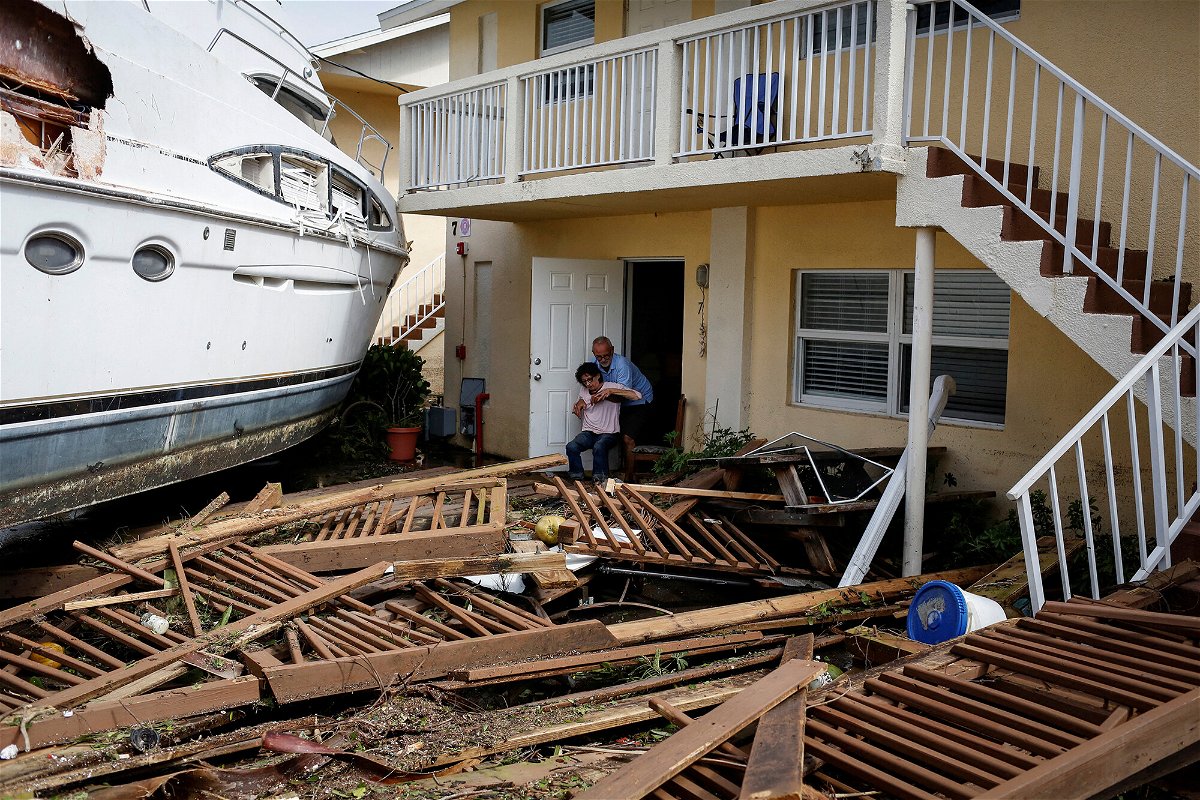 <i>Marco Bello/Reuters</i><br/>A man helps a woman next to a damaged boat amid a downtown condominium after Hurricane Ian caused widespread destruction in Fort Myers