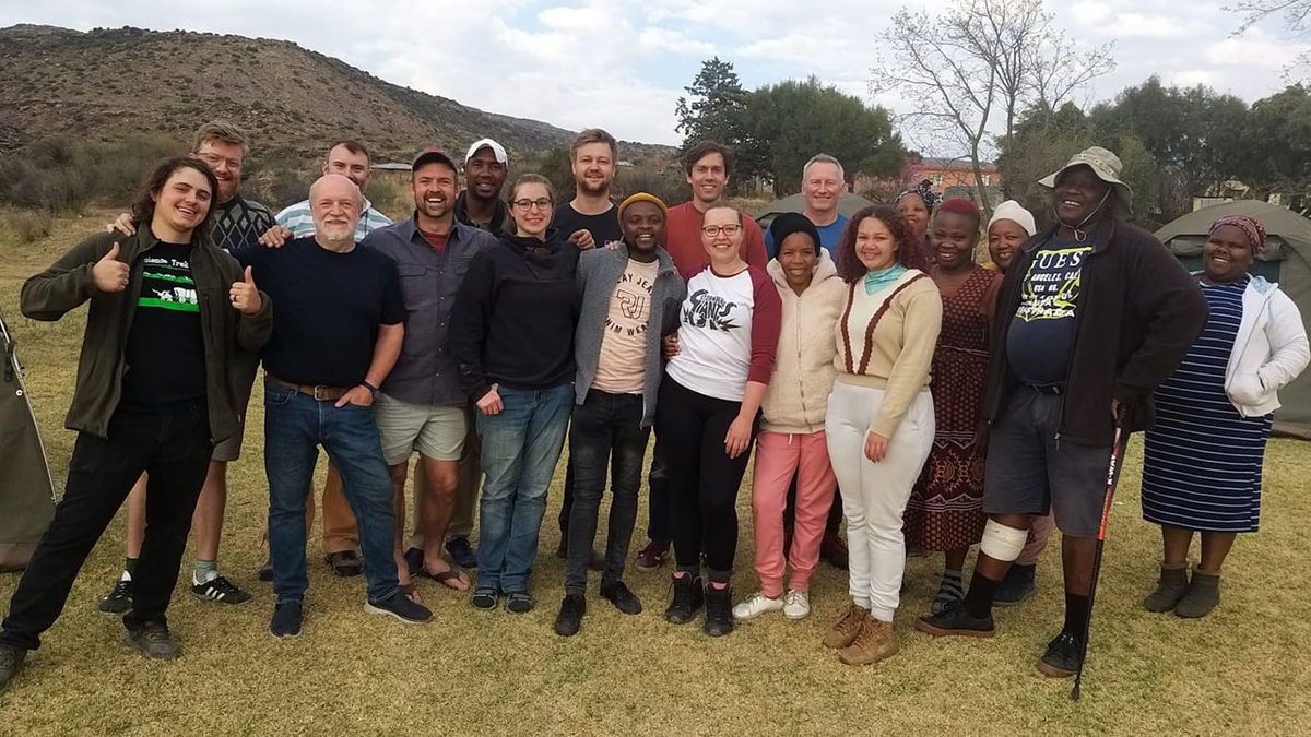 Xavier Jenkins, a doctoral student studying biology at Idaho State University, far left and giving a thumbs up, poses for a photo at a fossil dig site in South Africa with the local team as well as researchers from the University of Oxford, University of the Witwatersrand, University College London, and Natural History Museum in London. Over the summer, Jenkins spent four weeks in South Africa analyzing fossils.