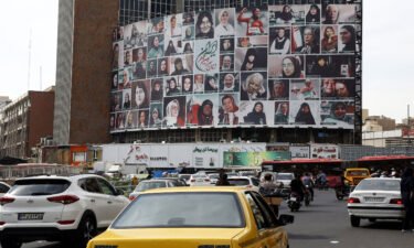 Iranians drive past a huge billboard showing a montage of pictures titled the women of my land