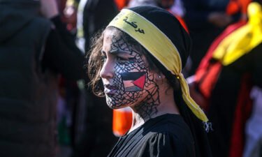 A girl with face-paint depicting the Palestinian flag looks on as others gather with flags of the Fatah movement during a rally to commemorate the 18th anniversary of the death of Palestinian leader Yasser Arafat