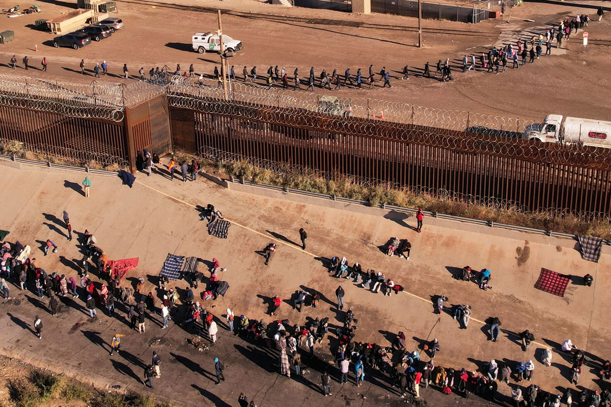 <i>Jose Luis Gonzalez/Reuters</i><br/>Migrants queue near the border wall after crossing the Rio Bravo river to turn themselves in to US Border Patrol agents to request asylum in El Paso