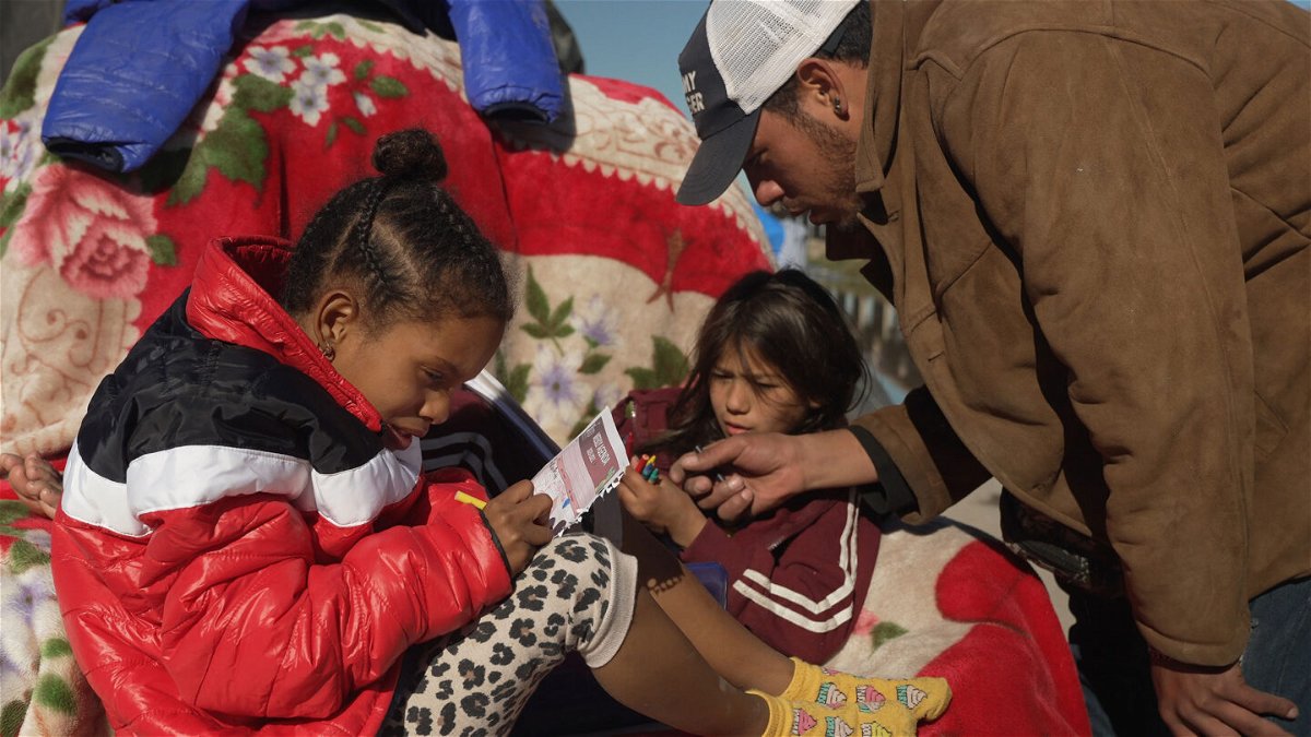 <i>David von Blohn/CNN</i><br/>Francisco Mota plays with his children at an improvised camp of migrants