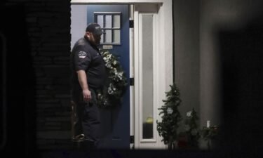 A law enforcement official stands at the front door of the Enoch