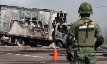 A soldier keeps watch near the wreckage of a truck set on fire by drug gang members in Sinaloa