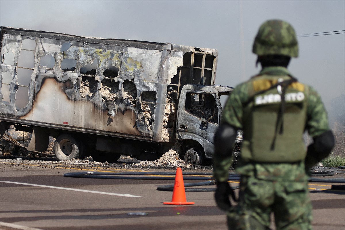 <i>Reuters</i><br/>A soldier keeps watch near the wreckage of a truck set on fire by drug gang members in Sinaloa