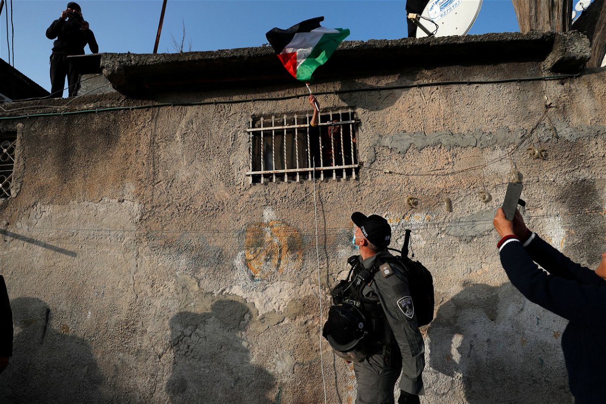 <i>Atef Safadi/EPA-EFE/Shutterstock</i><br/>A woman waves a Palestinian flag from her window during clashes with Israeli police in February of 2022.