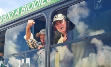 A man clenches his fist as he squeezes his upper body through the small window of a large bus leaving the Brazilian Federal Police Headquarters in Brasilia on January 10