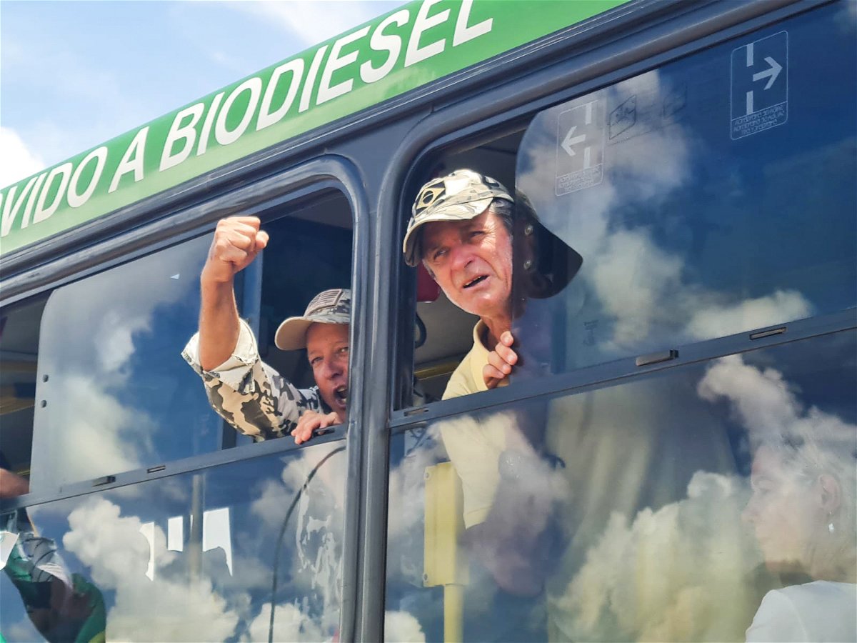 <i>Vasco Cotovio/CNN</i><br/>A man clenches his fist as he squeezes his upper body through the small window of a large bus leaving the Brazilian Federal Police Headquarters in Brasilia on January 10