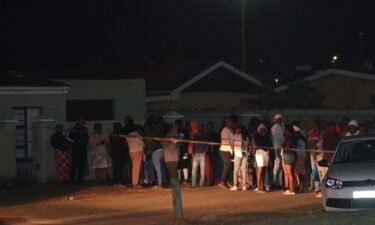 Bystanders wait behind a police tape marking the scene of a mass shooting in Gqeberha