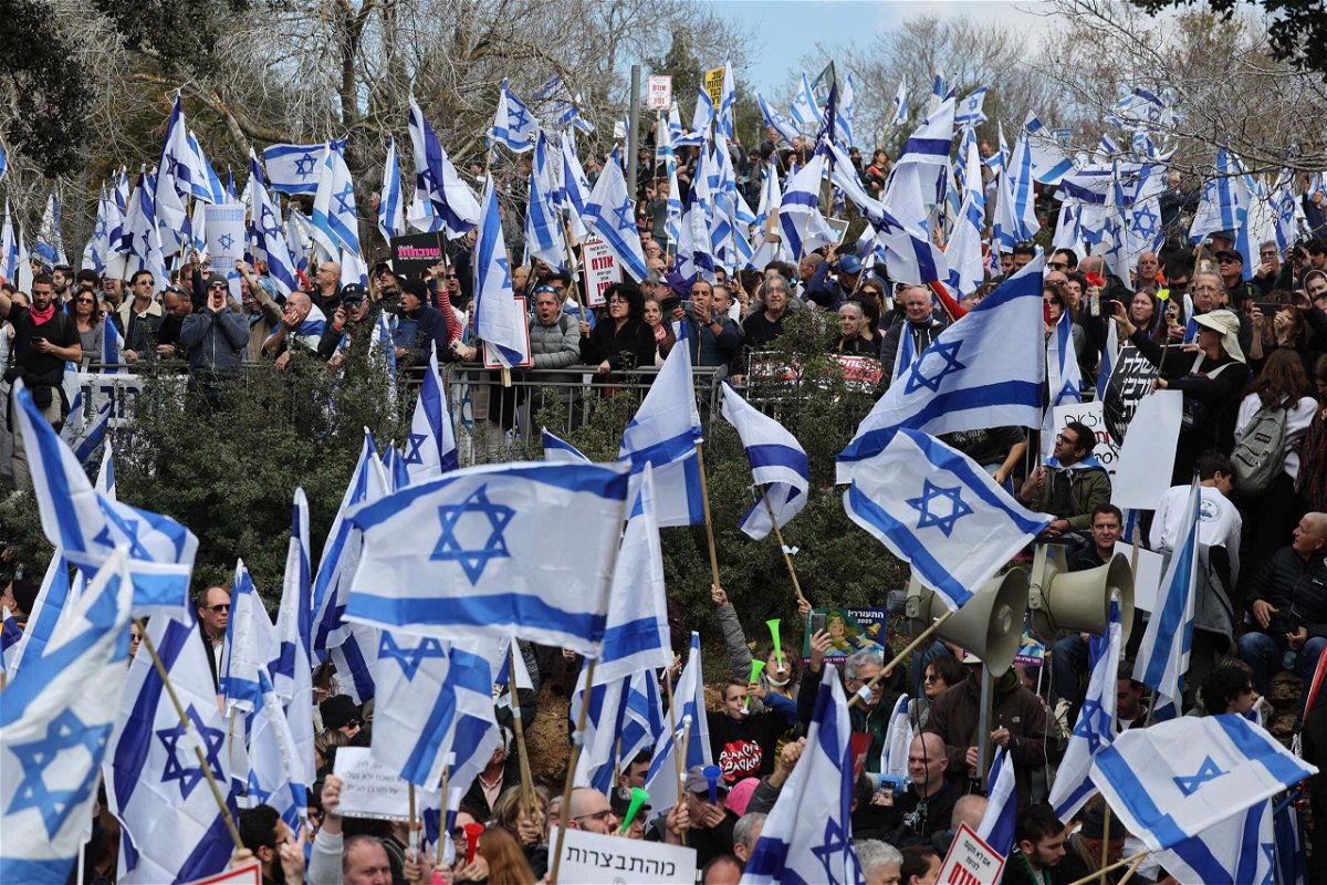 <i>Ahmad Gharabli/AFP/Getty Images</i><br/>Israeli protesters lift national flags and placards as they rally outside the Knesset in Jerusalem on Monday.