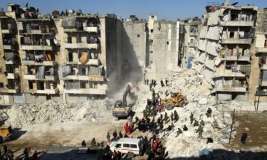 Syrian soldiers look on as rescuers use heavy machinery to sift through the rubble of a collapsed building in the northern city of Aleppo.
