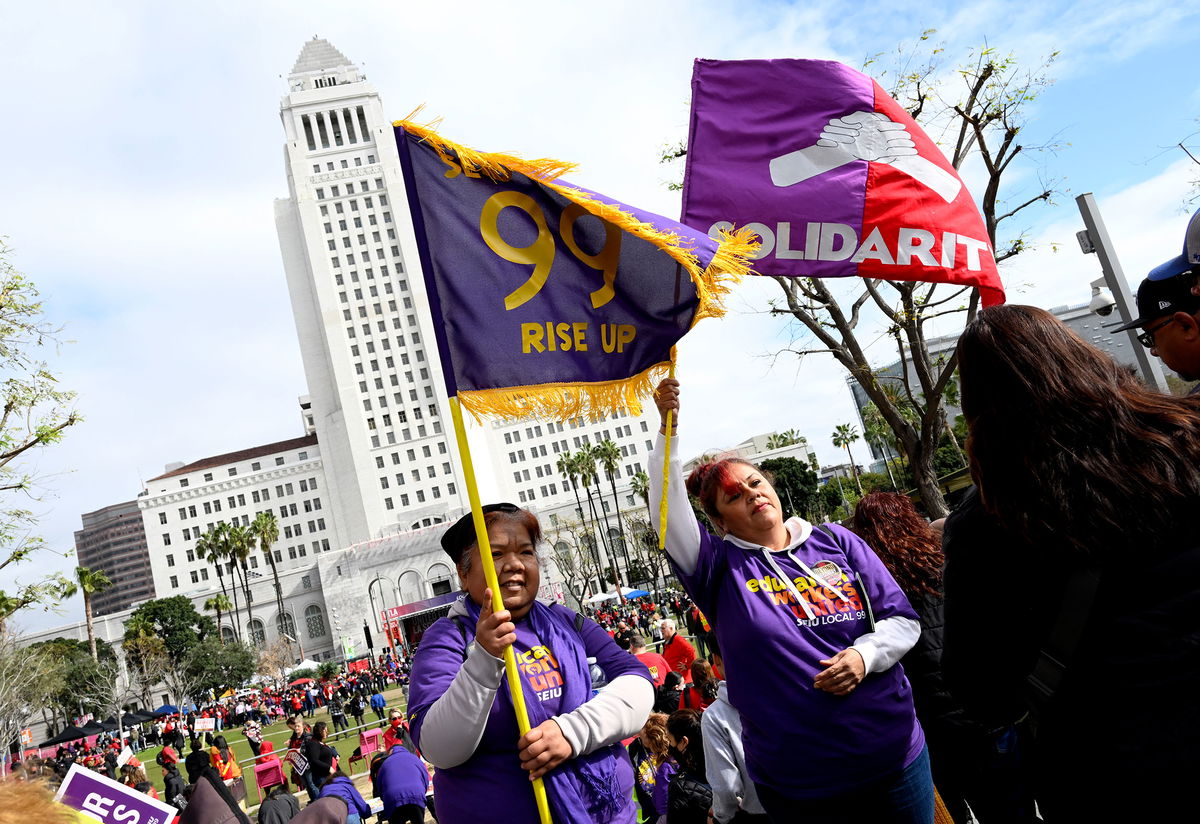 <i>Keith Birmingham/MediaNews Group/Pasadena Star-News/Getty Images</i><br/>Members of the school workers union hold up flags as thousands rally on March 15 in front of Los Angeles City Hall.