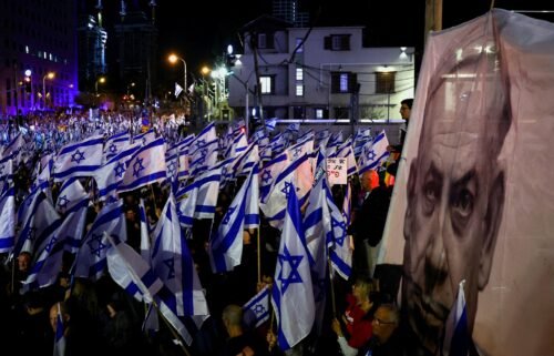 Demonstrators hold Israeli flags next to an image of Prime Minister Benjamin Netanyahu in Tel Aviv