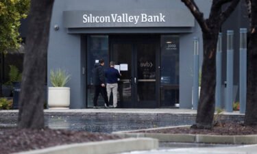A man puts a sign on the door of the Silicon Valley Bank as an onlooker watches at the bank's headquarters in Santa Clara