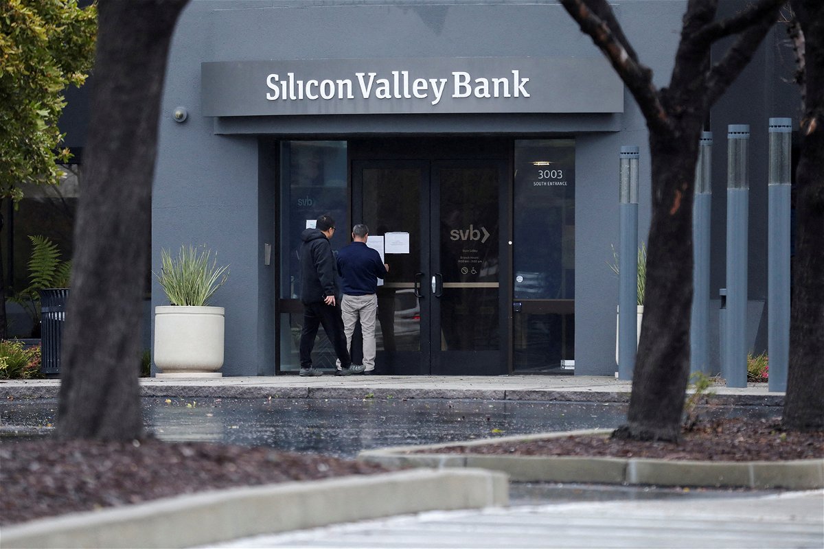 <i>Nathan Frandino/Reuters</i><br/>A man puts a sign on the door of the Silicon Valley Bank as an onlooker watches at the bank's headquarters in Santa Clara