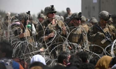 US soldiers stand guard behind barbed wire as Afghans sit on a roadside near the military part of the airport in Kabul on August 20