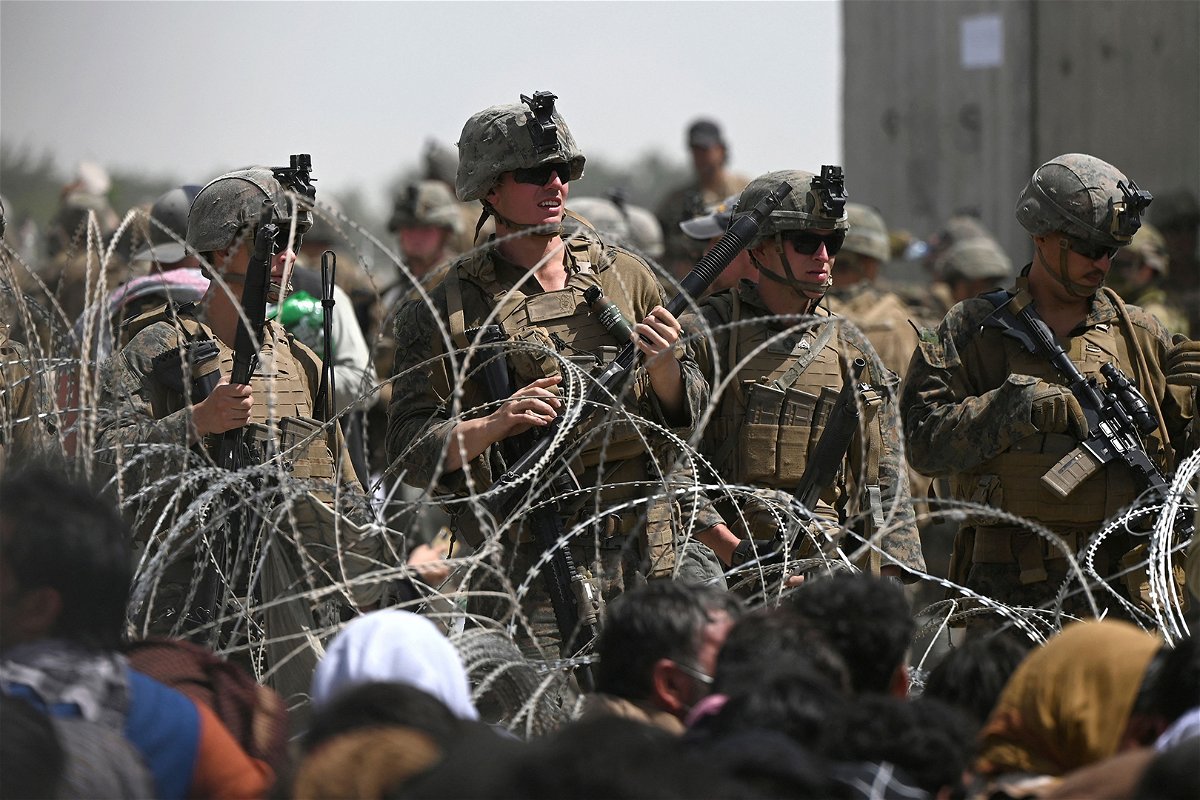 <i>Wakil Kohsar/AFP/Getty Images</i><br/>US soldiers stand guard behind barbed wire as Afghans sit on a roadside near the military part of the airport in Kabul on August 20