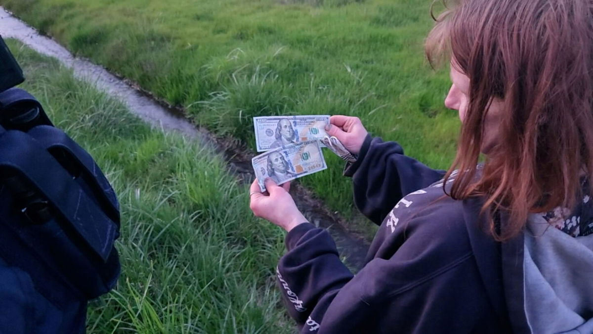 <i>KEZI</i><br/>A woman holds cash on the side of Interstate-5 after a man tossed bills from his car in Oregon on April 11.