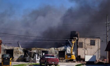 Workers knock down a section of site of an industrial fire the area as smoke billows from the site in Richmond