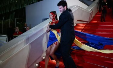 A protester wearing a dress in the colors of the Ukrainian flag is detained by security after she covered herself in fake blood at Cannes Film Festival.
