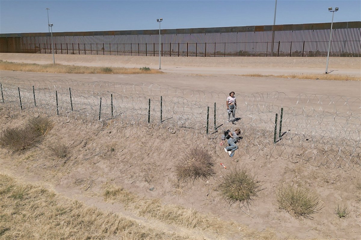 <i>Evelio Contreras/CNN</i><br/>A woman helps a companion crawl through newly installed barbed wire at the US border.