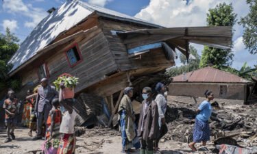 People walk next to a house destroyed by the floods in the village of Nyamukubi