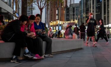 Women watch a video on a mobile phone in a busy retail shopping area in Beijing