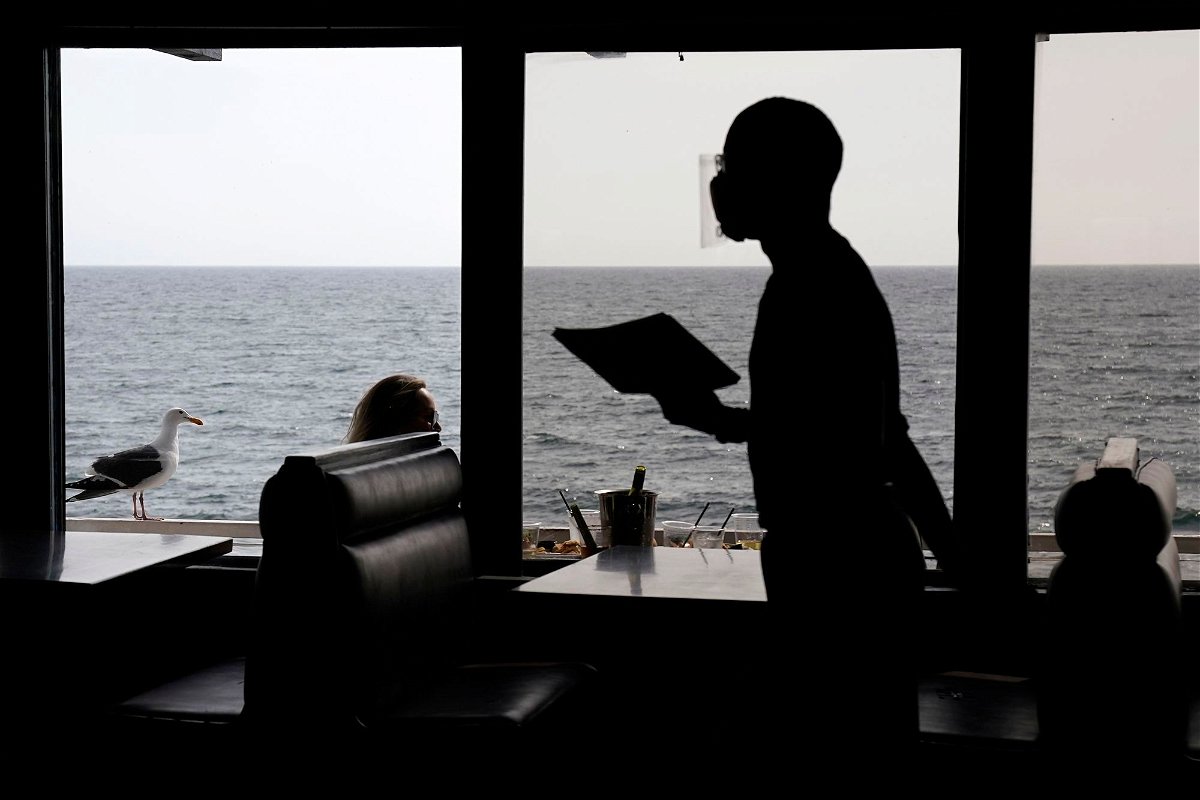<i>Mark J. Terrill/AP/FILE</i><br/>A waiter walks through an empty dining room as diners eat outside in front of beach views at Gladstone's restaurant in 2021