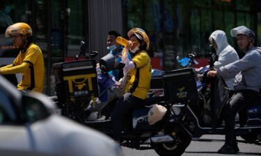 A delivery rider drinks water as she and other motorists wait to cross a street on a hot day in Beijing