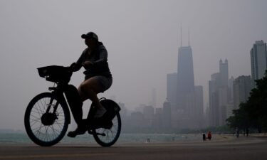 A person rides a bicycle along the shore of Lake Michigan as the downtown skyline is blanketed in haze from Canadian wildfires on June 27 in Chicago.