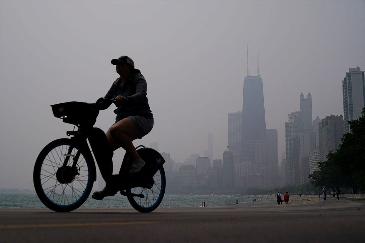 <i>Kiichiro Sato/AP</i><br/>A person rides a bicycle along the shore of Lake Michigan as the downtown skyline is blanketed in haze from Canadian wildfires on June 27 in Chicago.