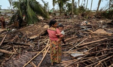 A Rohingya woman carries her baby next to her destroyed house at Basara refugee camp in Sittwe on May 16 after cyclone Mocha made landfall.