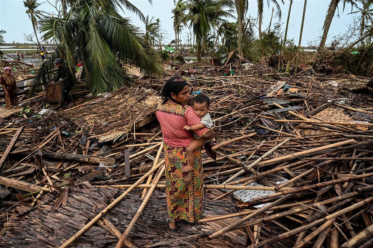 <i>Sai Aung Main/AFP/Getty Images</i><br/>A Rohingya woman carries her baby next to her destroyed house at Basara refugee camp in Sittwe on May 16 after cyclone Mocha made landfall.