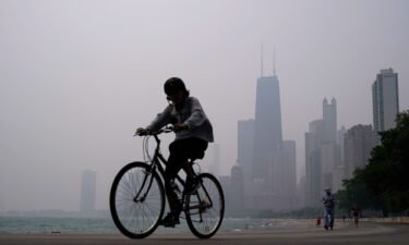 A person rides a bicycle along the shore of Lake Michigan as the downtown skyline is blanketed in haze from Canadian wildfires on June 27 in Chicago.