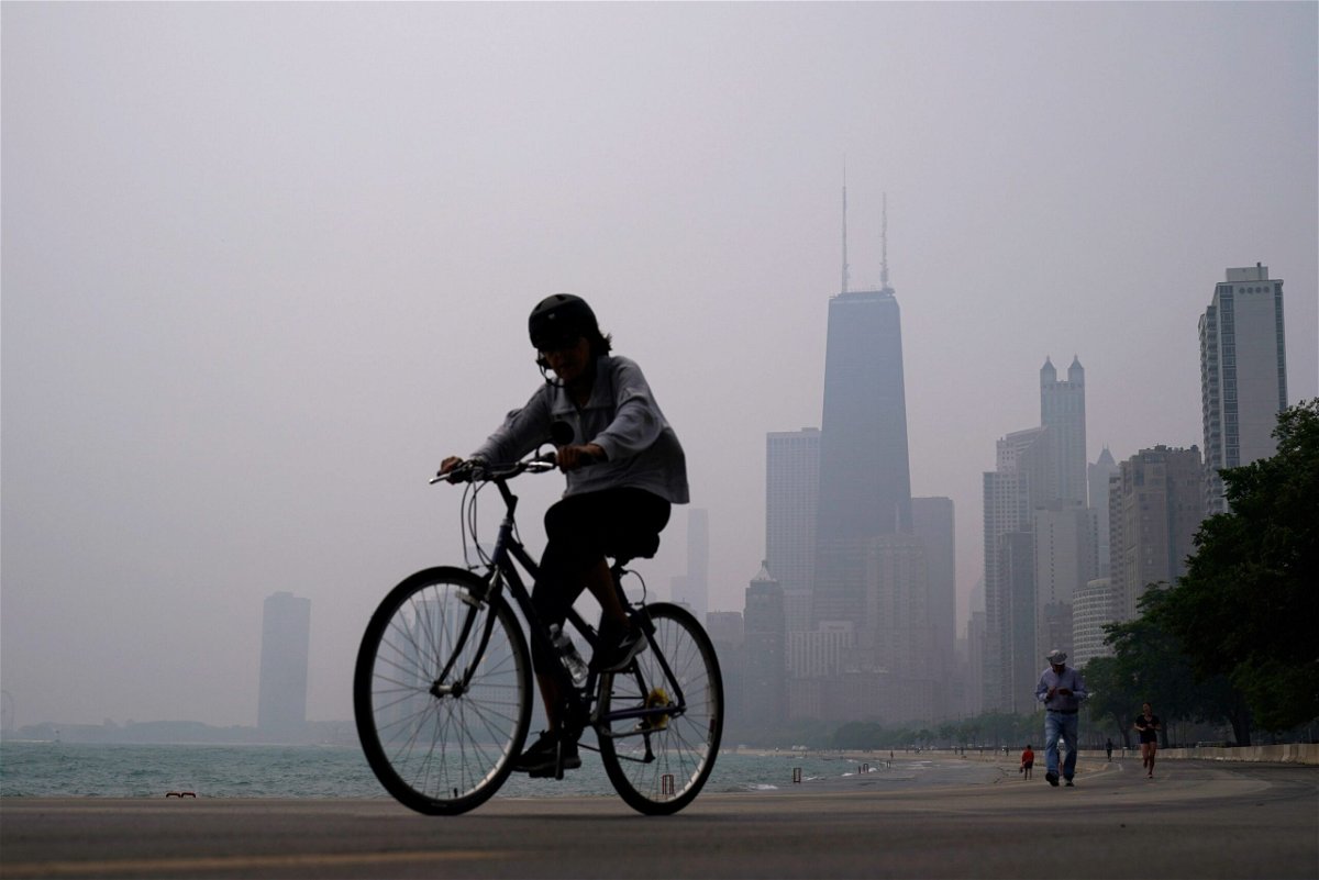 <i>Kiichiro Sato/AP</i><br/>A person rides a bicycle along the shore of Lake Michigan as the downtown skyline is blanketed in haze from Canadian wildfires on June 27 in Chicago.