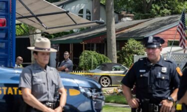 New York State police officers stand guard as law enforcement searches the home of Rex Heuermann