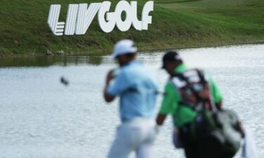 A golfer and caddie walk by LIV Golf signage during the team championship stroke-play round of the LIV Golf Invitational - Miami at Trump National Doral Miami on October 30