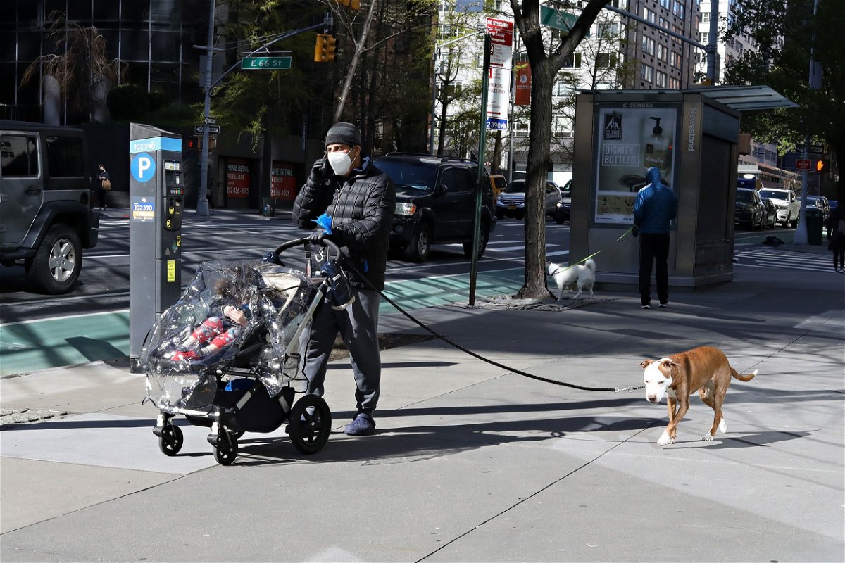 <i>Cindy Ord/Getty Images</i><br/>A man speaks on a phone while pushing a child in a stroller and walking a dog on April 20