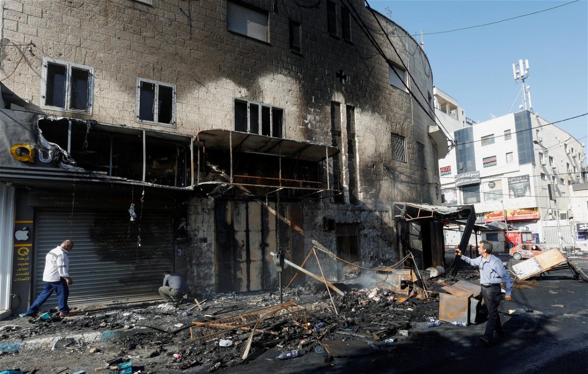 <i>Mohamad Torokman/Reuters</i><br/>People walk past debris and a building damaged amid an Israeli military operation