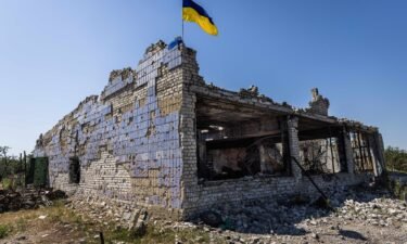 A Ukrainian flag waves above a destroyed building after shelling in Vremivka
